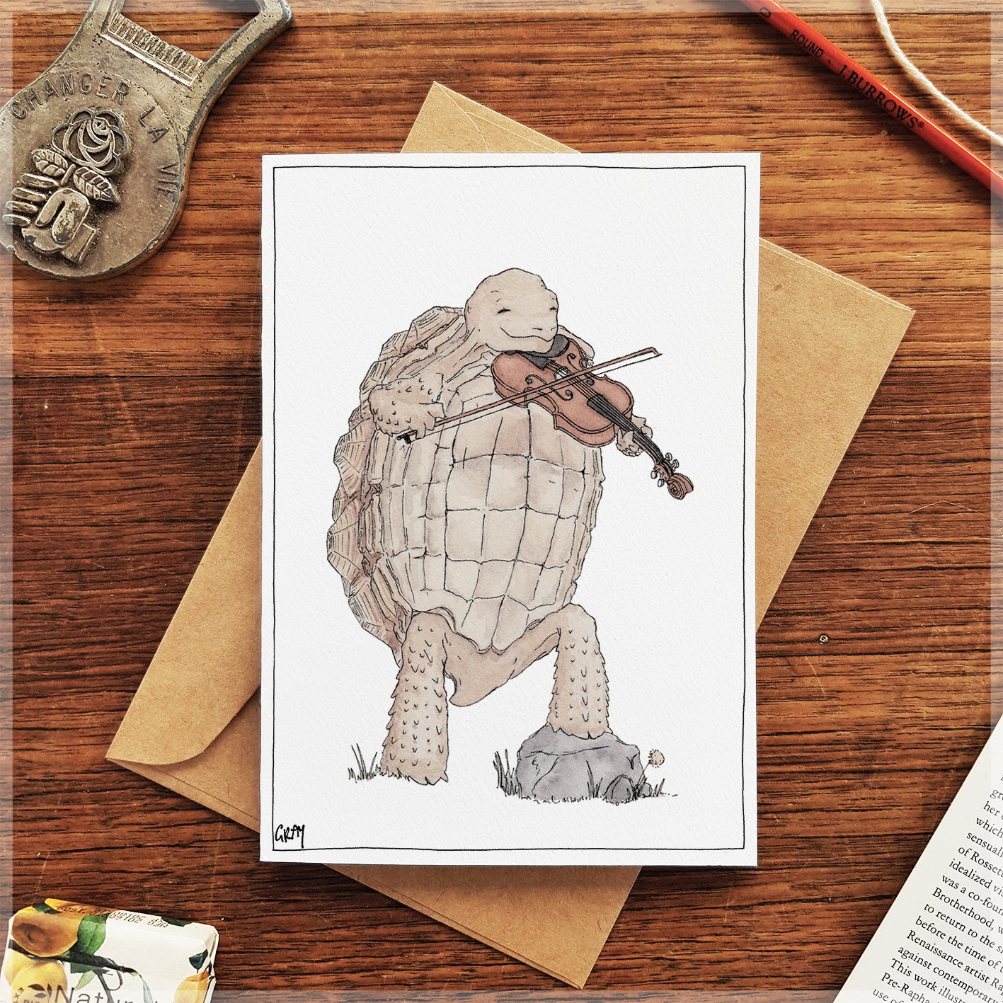 Card with a tortoise playing a violin on a wooden surface with an envelope.