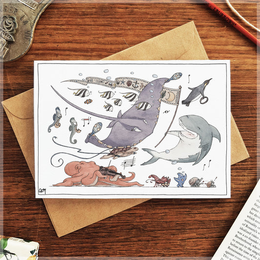 Illustrated card with sharks and musical elements on a wooden surface with an envelope.