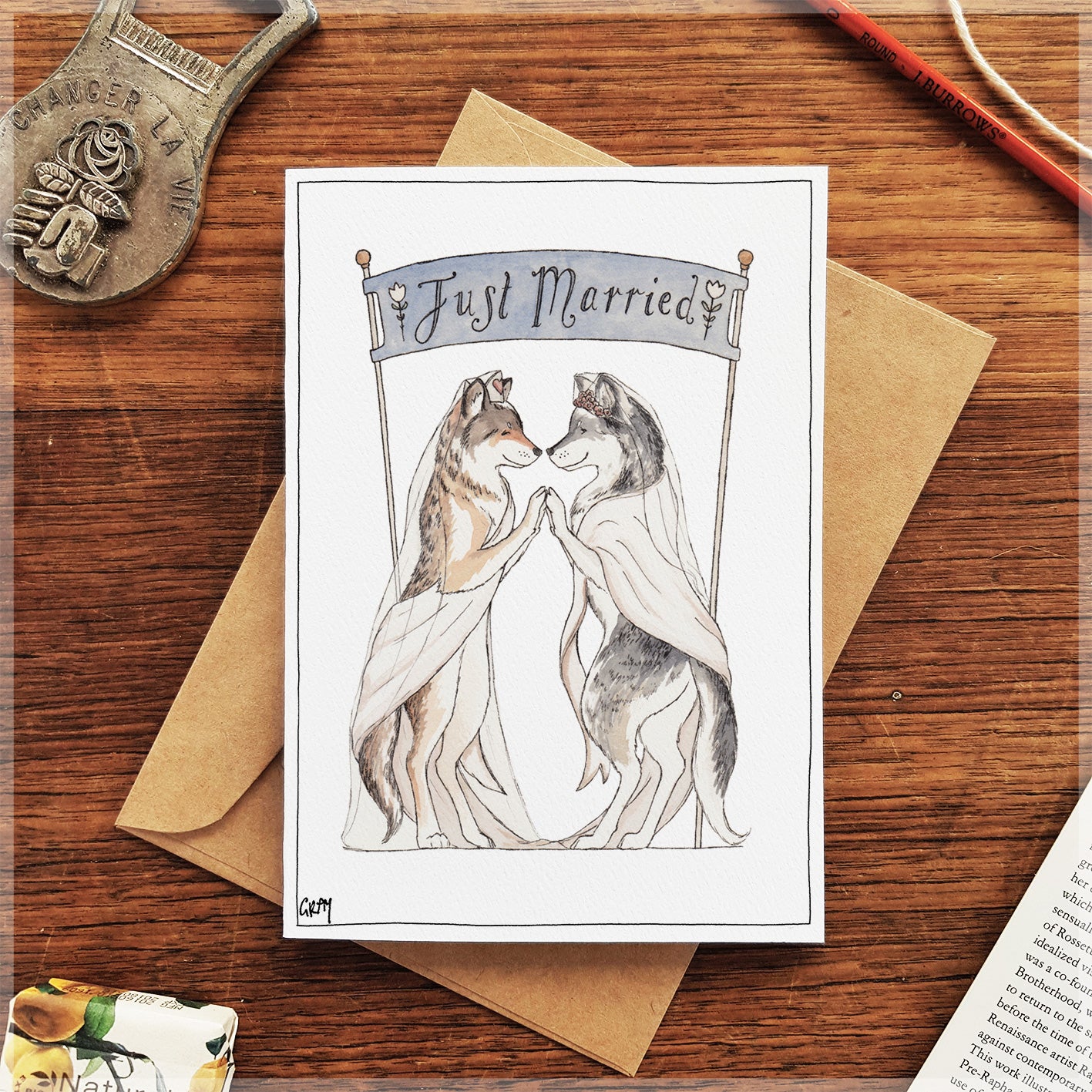 Wedding card with two wolves holding hands and 'Just Married' banner on a wooden surface.
